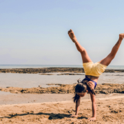 Ein Mädchen in gelber Shorts macht Handstand am Meer