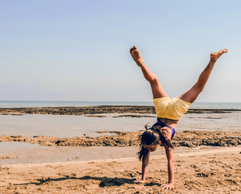 Ein Mädchen in gelber Shorts macht Handstand am Meer
