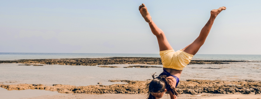 Ein Mädchen in gelber Shorts macht Handstand am Meer